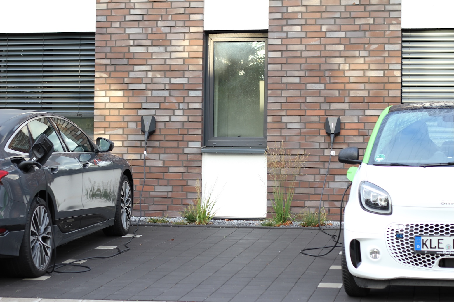 Zwei Elektroautos laden an fest installierten Wallboxen vor einem modernen Wohngebäude