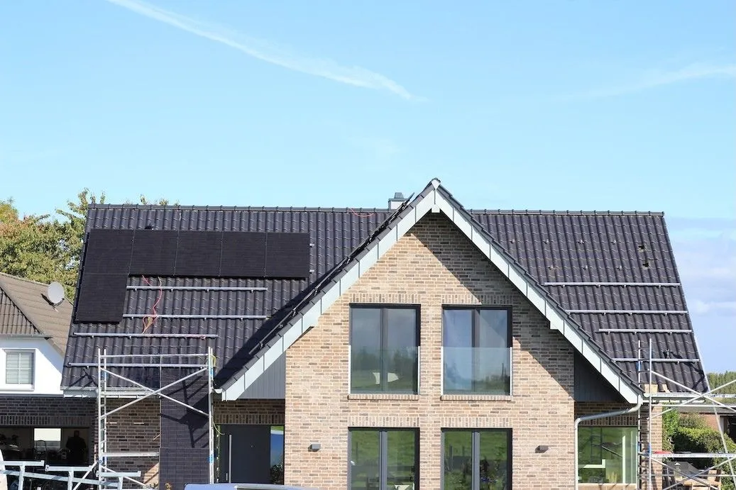 „Zweering-Monteur installiert Photovoltaikmodule auf einem Ziegeldach eines Einfamilienhauses mithilfe eines Gerüsts.“