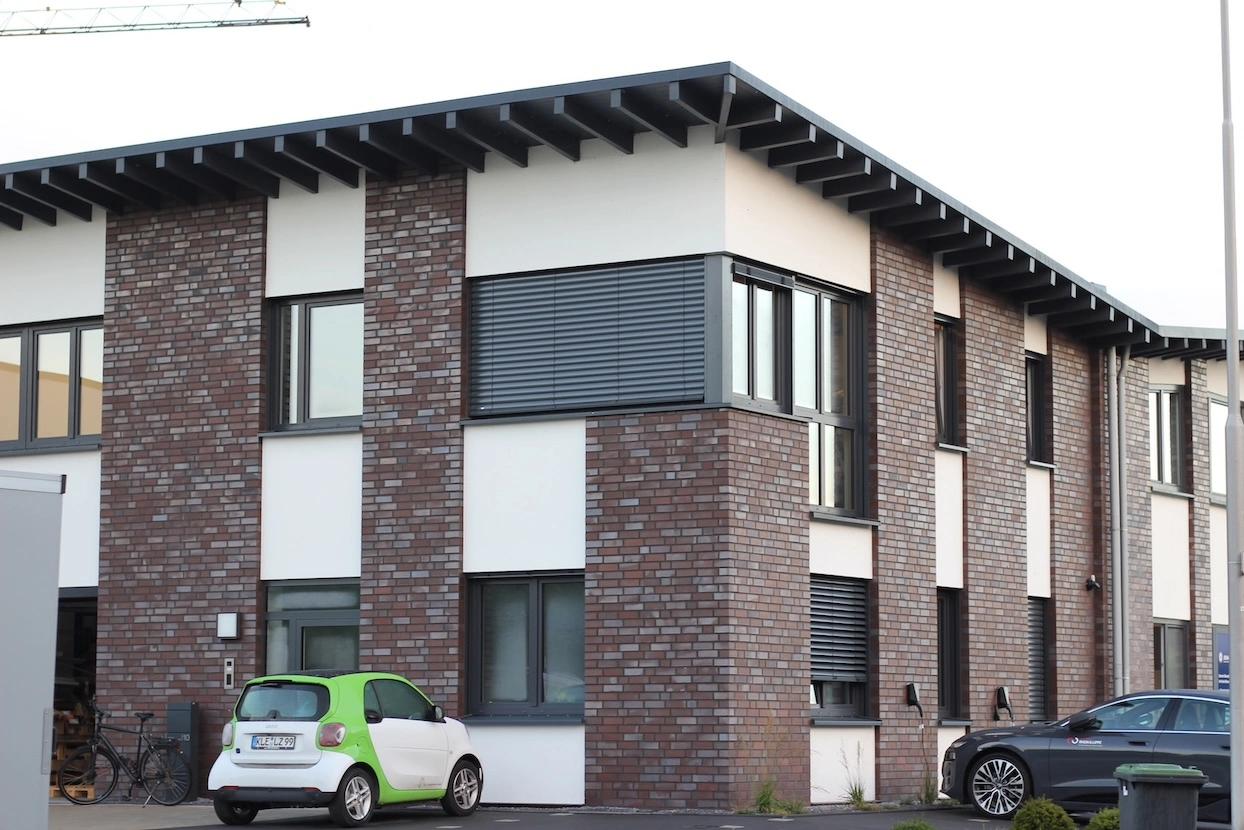 „Moderne Firmenfassade von Zweering Elektrotechnik mit Klinkeroptik, großen Fenstern und Kundenfahrzeugen.“