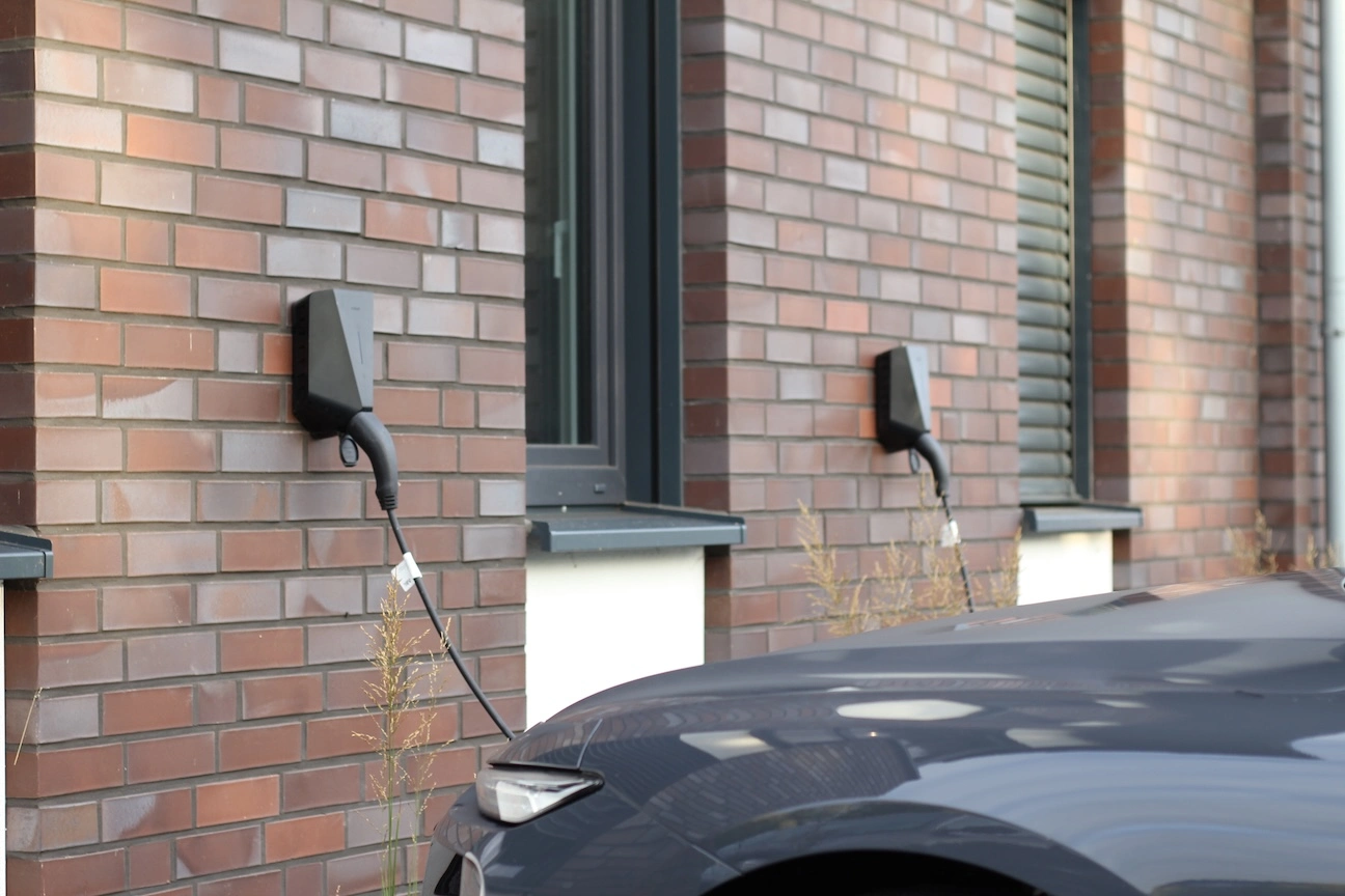 „Elektrisches Fahrzeug an zwei Wallbox-Ladestationen eines modernen Wohngebäudes, installiert von Zweering Elektrotechnik.“