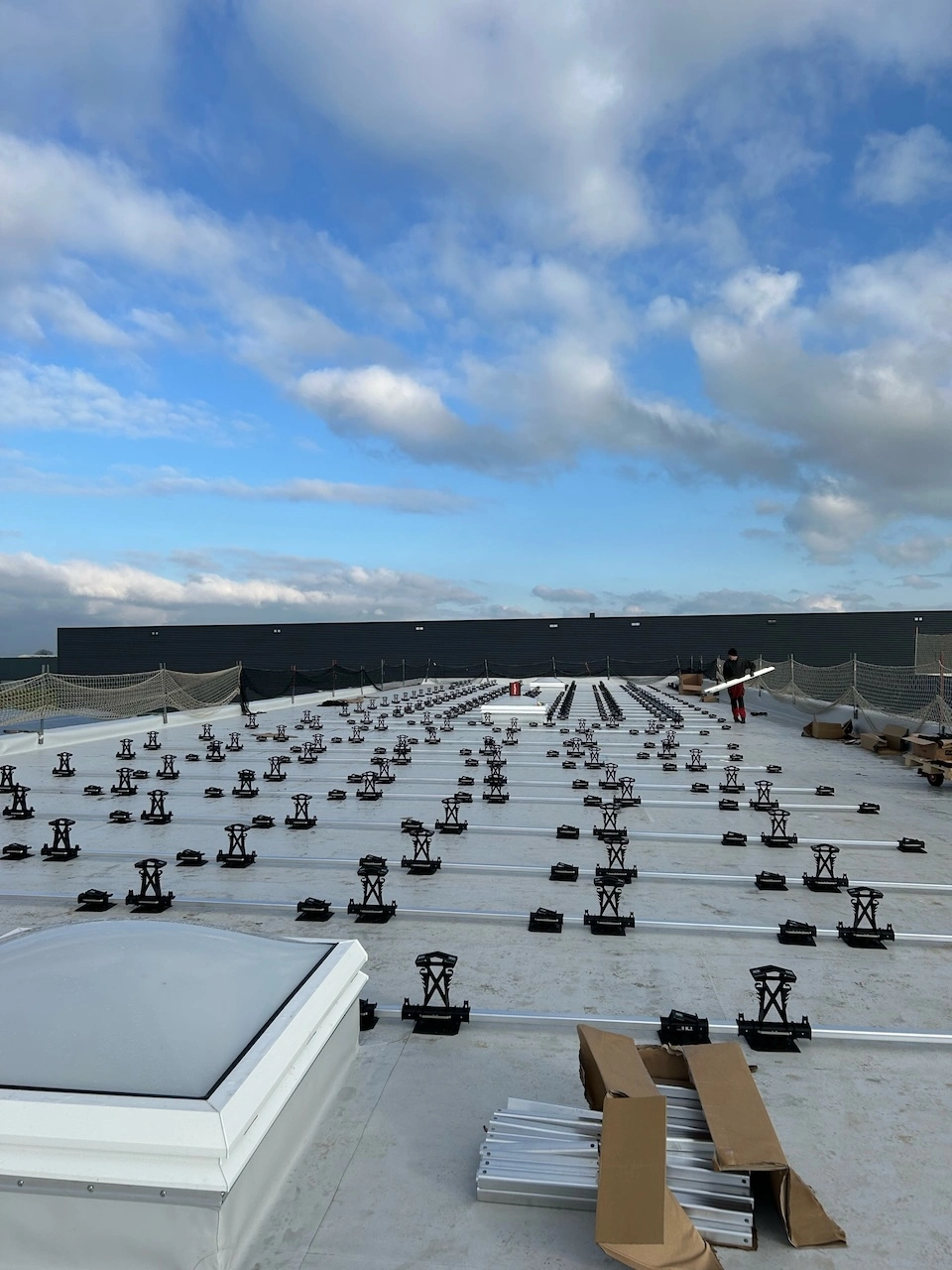 „Montage einer großflächigen Photovoltaik-Unterkonstruktion auf einem Industrie-Flachdach vor blauem Himmel.“