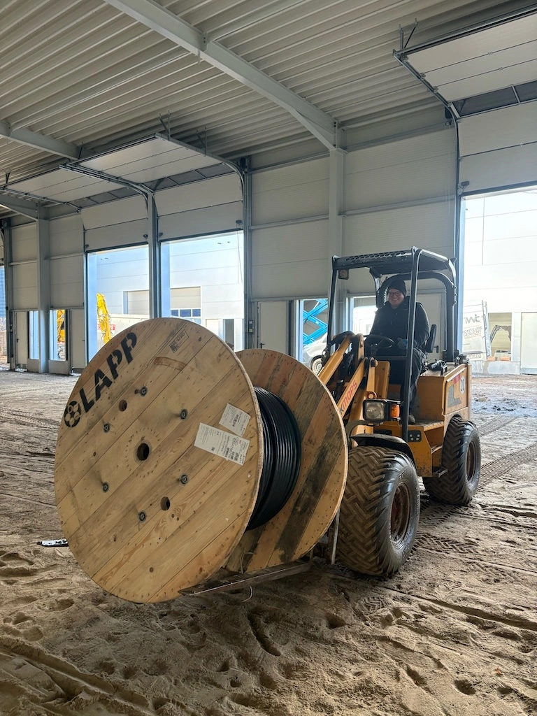 „Zweering-Mitarbeiter transportiert eine große Kabeltrommel mit einem Radlader in einer Industriehalle.“