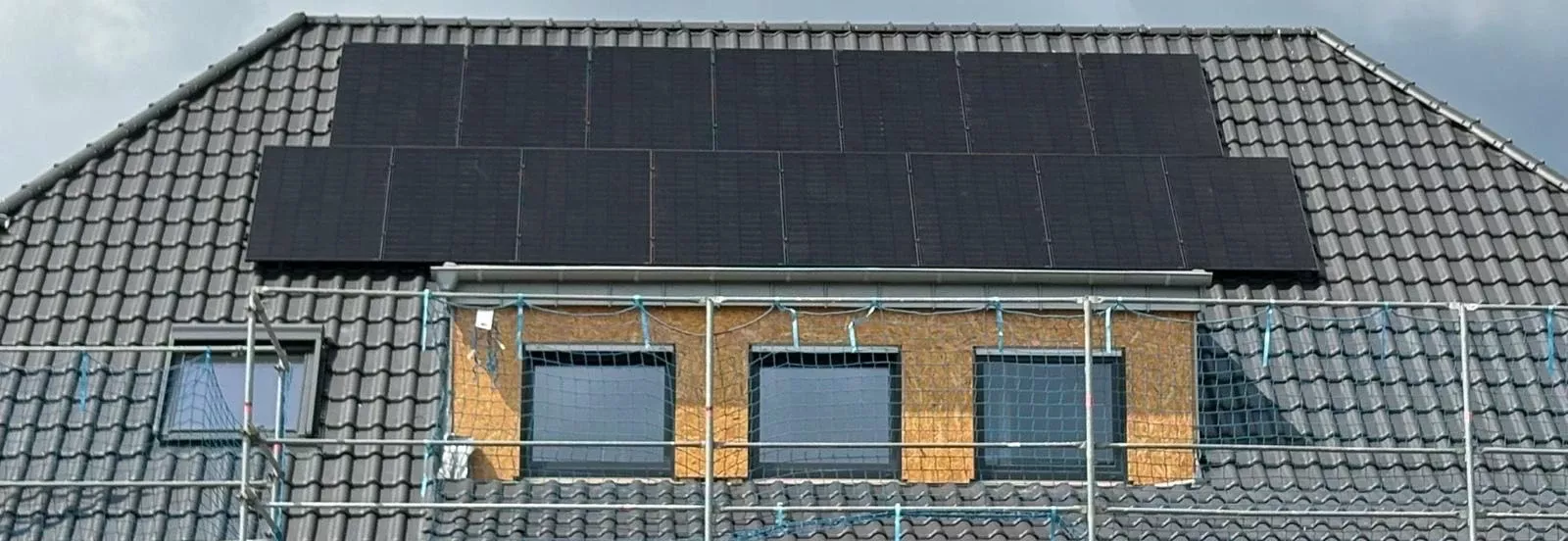 „Montage einer großflächigen Photovoltaikanlage auf einem Wohnhausdach während der Bauphase.“